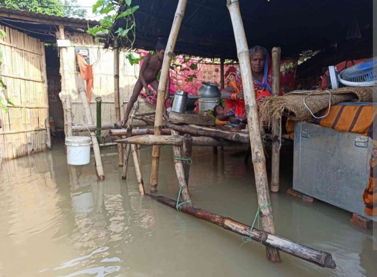बाढ़ के पानी में डूबे घर के अंदर चौकी पर बैठा परिवार